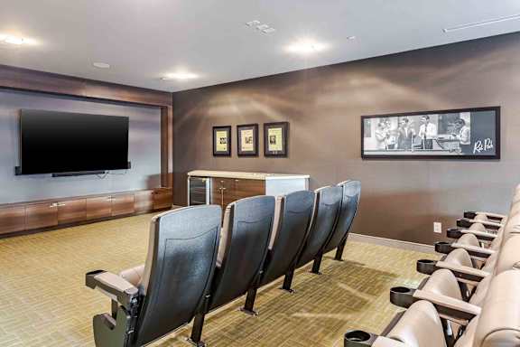 A row of black chairs are lined up in front of a wall with a television and picture frames.