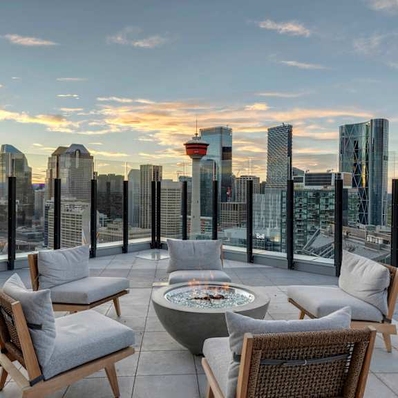A rooftop patio with a fire pit and chairs overlooking a city skyline.