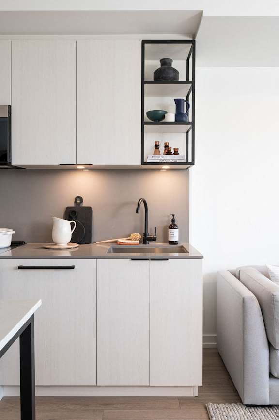 A modern kitchen with white cabinets and a black shelf above the sink.