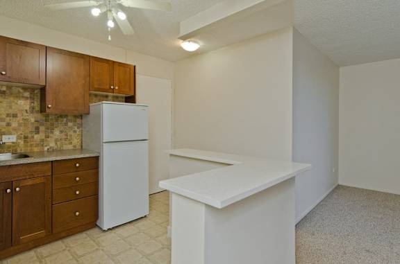 A kitchen with a white refrigerator, brown cabinets, and a white countertop.