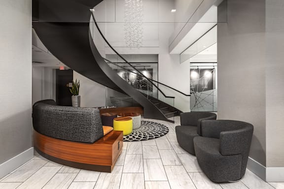 A modern living room with a curved sofa, armchairs, and a staircase at Clayton on the Park Apartments, Clayton 63105