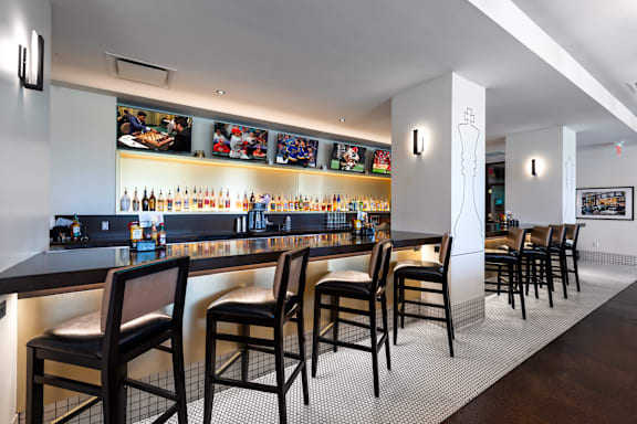 A bar with black chairs and a counter with bottles on it at Clayton on the Park Apartments, Missouri
