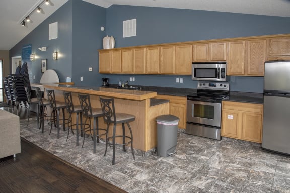 a kitchen with wooden cabinets and a bar with chairs and a refrigerator