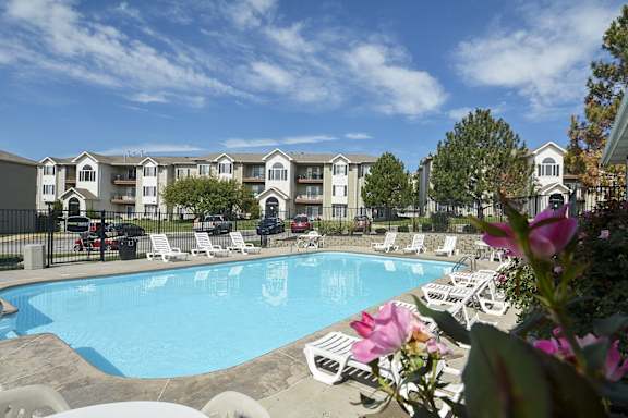 an outdoor swimming pool with white chairs and apartments in the background