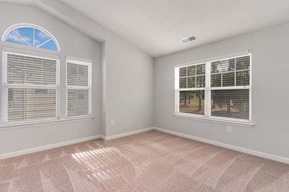 A room with a carpeted floor and two windows.