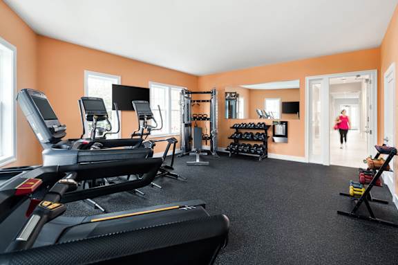 A woman is walking in a gym with treadmills, weights, and other exercise equipment.