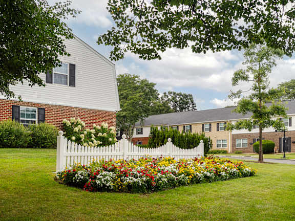 A white picket fence with a flower bed in front of a house.