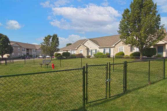 A black fence surrounds a green field with houses in the background.
