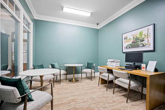 A room with a desk, chairs, and a framed picture of a car on the wall.