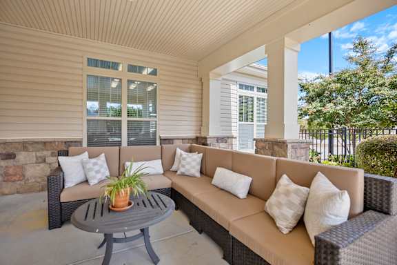 A patio with a couch, pillows and a table.