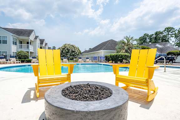 Two yellow chairs are placed on a patio next to a fire pit.