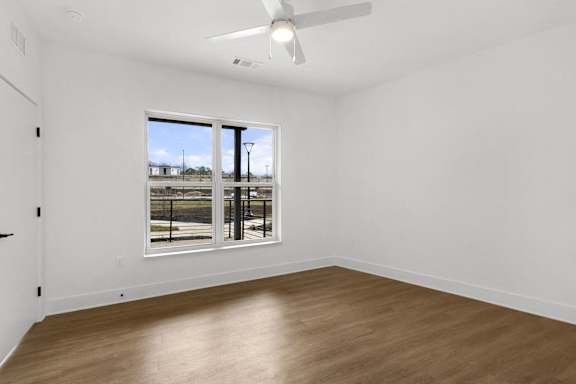 A room with a ceiling fan and a large window overlooking a parking lot.