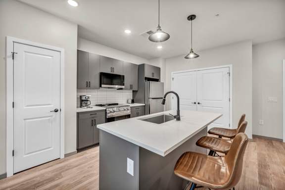 A modern kitchen with a large island and brown chairs.