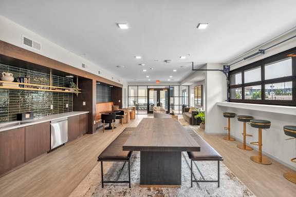 A modern kitchen with a long wooden table in the middle.