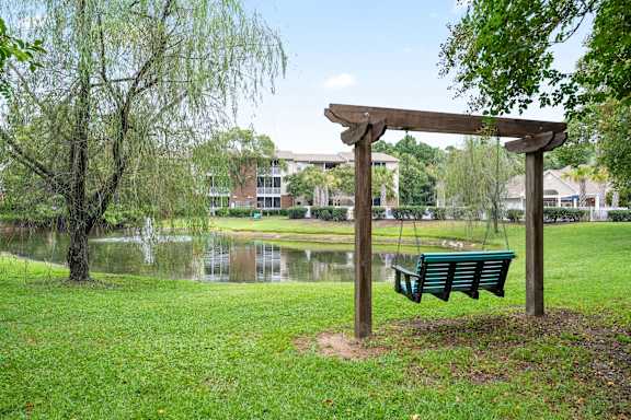 A wooden swing set sits in a grassy area next to a pond at Litchfield Oaks Apartments in Pawleys Island, South Carolina, 29585