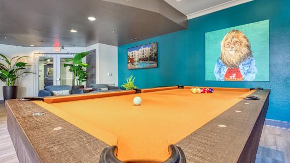 A pool table with a painting of a lion on the wall.