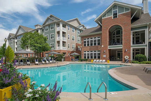 A large swimming pool is surrounded by a yellow planter box with purple and white flowers.