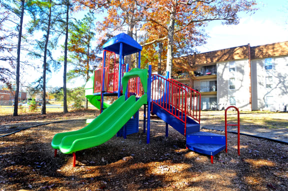 a playground with a green and red slide and a blue and red swing set