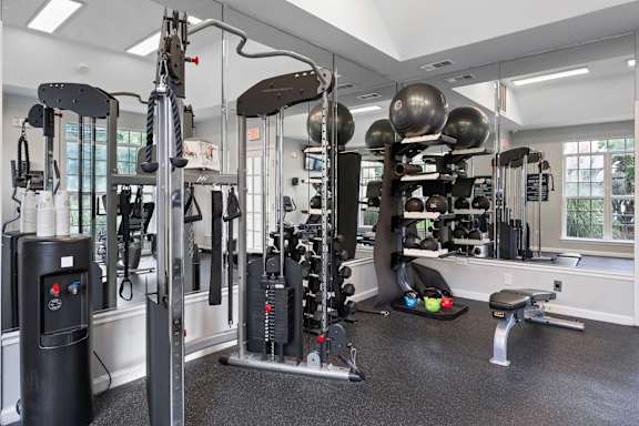 A gym with a variety of equipment including a weight bench, a leg press machine, and a cable machine at Litchfield Oaks Apartments in Pawleys Island, 29585
