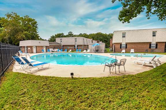 A pool surrounded by lawn chairs and trees.