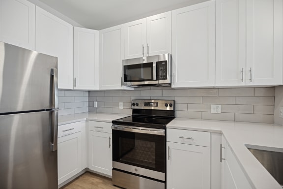 an all white kitchen with stainless steel appliances and white cabinets at Centro at Pine Nash in Wilson, North Carolina