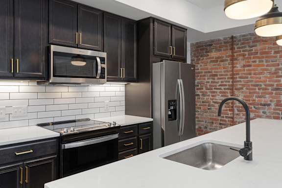 A kitchen with black cabinets and a brick wall.