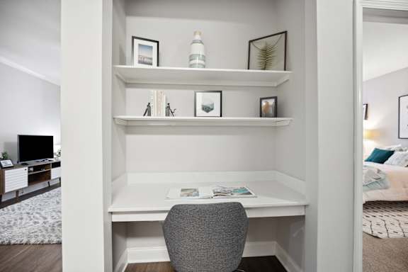 A white desk with a grey chair in a room with a white wall.