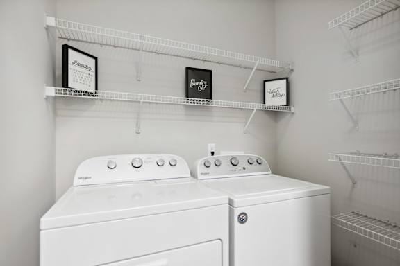 Two white washing machines in a laundry room with shelves above them.