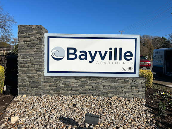 A property sign for Bayville Apartments is displayed in front of a stone wall.