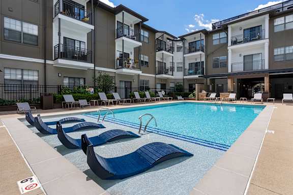 A swimming pool with lounge chairs in front of apartment buildings.
