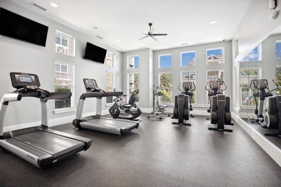 the gym with treadmills and other exercise equipment in a building with windows