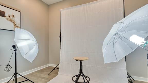 A photography studio with a white backdrop, a light stand, and a stool.