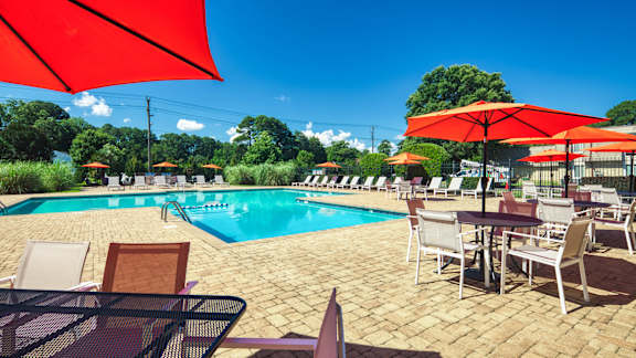 a swimming pool with tables and chairs and umbrellas at Bayville Apartments in Virginia Beach, VA 23455
