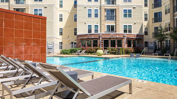 A pool with sun loungers and a red wall.