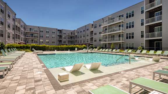 A large outdoor swimming pool surrounded by lounge chairs and buildings.