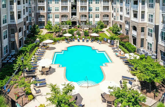 A large swimming pool surrounded by lounge chairs and umbrellas in a courtyard surrounded by apartment buildings.