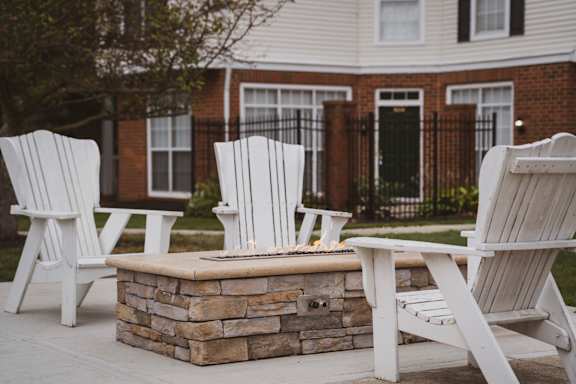 Three white chairs are arranged around a stone fire pit at The Orchard, Dublin, OH