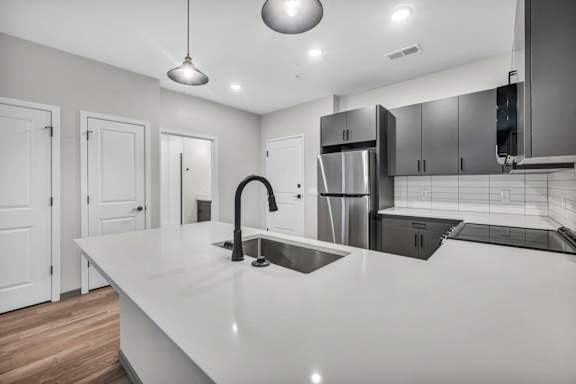 A modern kitchen with a long white countertop and stainless steel appliances.
