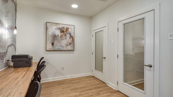 A room with a wooden table and chairs, a painting on the wall, and a door with a glass panel.