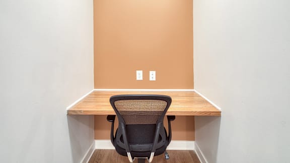 A black chair is in front of a desk with a light switch on the wall.