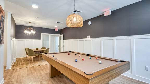 A pool table with balls set up for a game in a room with a wooden floor and a ceiling light.