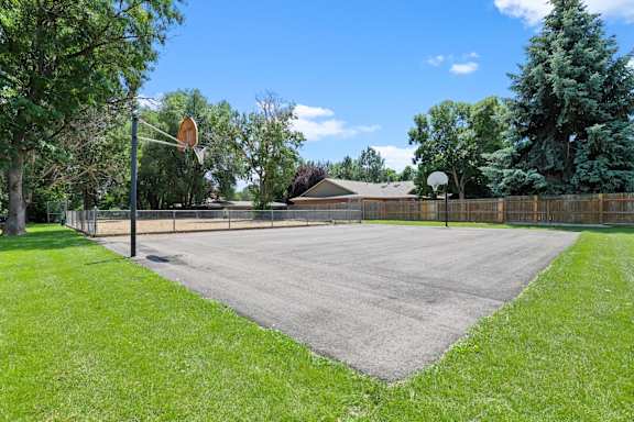 A basketball court surrounded by a fence and trees.