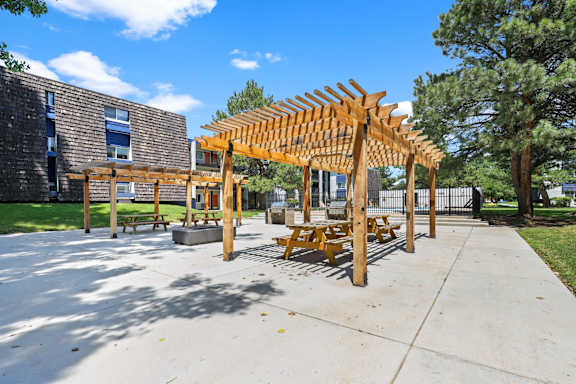 A wooden pavilion with benches is situated in a courtyard.