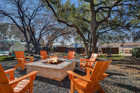 Concrete fire pit surrounded by orange adirondack chairs at Peaks @ NW Hills Apartments, Austin, 78731