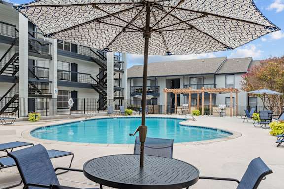 Poolside table with umbrella and aqua blue pool at Peaks at Live Oak Apartments, Texas