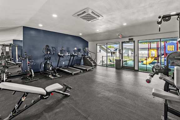 Fitness center with treadmills and glass doors overlooking playground at Peaks at Live Oak Apartments, San Antonio