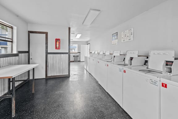 Laundry room with multiple washers and folding table at Peaks at Live Oak Apartments, San Antonio, TX