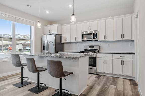 a kitchen with white cabinets and a bar with two chairs