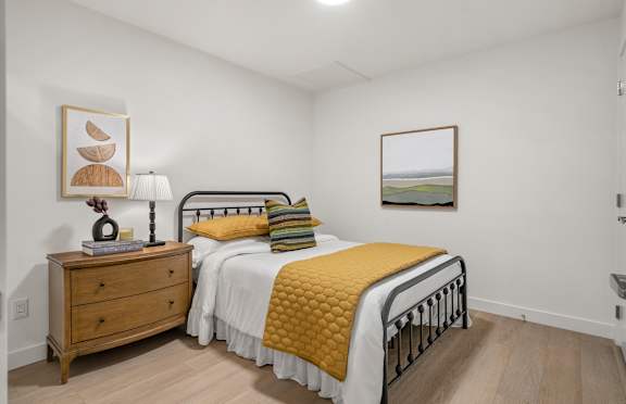 A bedroom with a bed, nightstand, and two pictures on the wall.