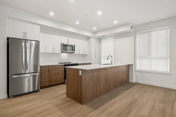 A modern kitchen with a refrigerator, microwave, and wooden cabinets.